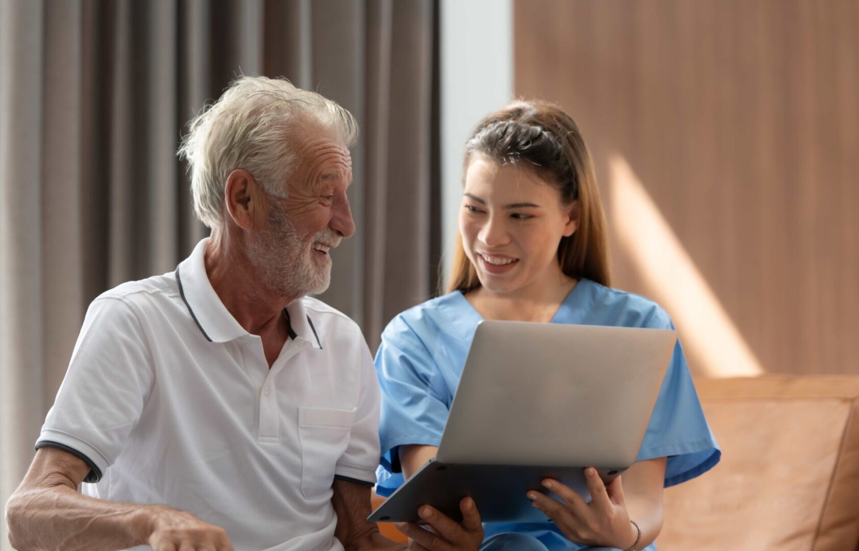 Caregiver shows senior man laptop screen.